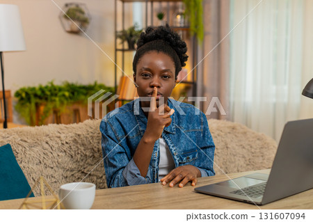 African American young woman shows silence secret gesture with finger to lips hinting secret at home 131607094