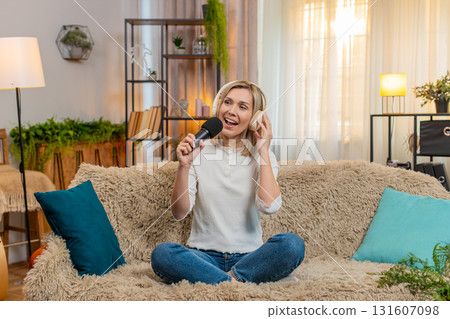 Adult woman singing with headphones and microphone at home dancing joyfully feeling like a superstar 131607098