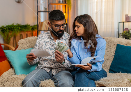Indian family couple man woman calculating bills money at home, making notes reacting frustration Indian family couple man woman calculating bills money at home, making notes reacting frustration 131607128