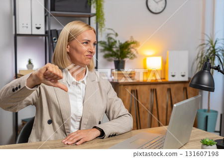 Upset mature businesswoman working on laptop showing thumbs down sign gesture at home office desk 131607198