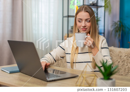 Caucasian woman freelancer working remotely sitting at home table typing on laptop drinking coffee Caucasian woman freelancer working remotely sitting at home table typing on laptop drinking coffee 131607203
