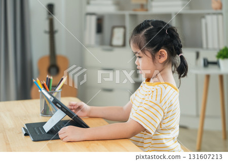 Young girl engaged in online learning at home, using tablet with focused expression, bright room with natural light, creative workspace atmosphere 131607213