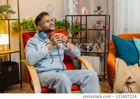 Attractive smiling Indian man drinking a cup of coffee or herbal tea at home chair in the morning 131607224