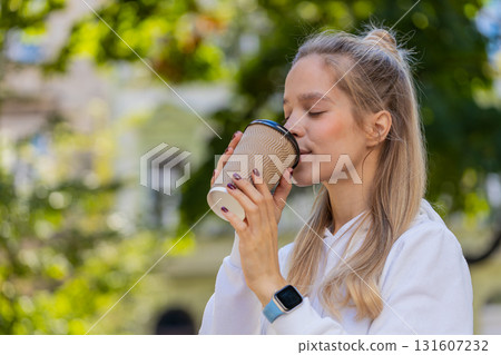Happy young Caucasian woman enjoying drinking morning coffee hot drink and smiling on city street 131607232
