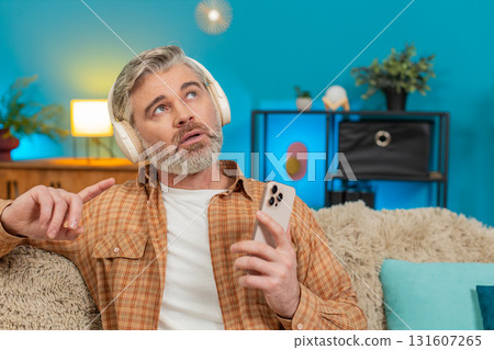 Mature man sitting on sofa with wireless headphones, enjoying audiobook and online learning at home 131607265