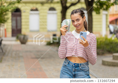 Happy woman counting money dollar cash, use smartphone calculator app in urban city street Happy woman counting money dollar cash, use smartphone calculator app in urban city street 131607294