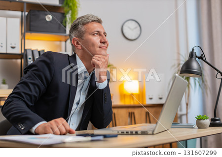 Handsome young businessman thinking business ideas while sitting with laptop at home office desk 131607299