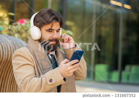 Happy Indian man in wireless headphones listening music in smartphone dancing sitting on bench 131607352