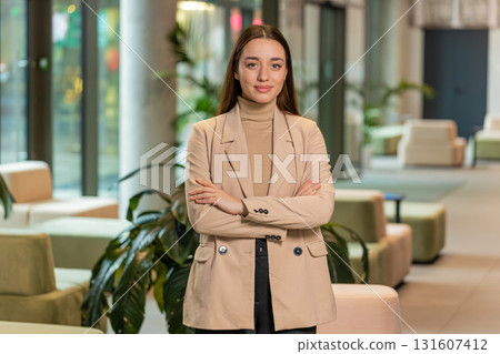 Portrait of happy young businesswoman with arms crossed looking at camera in office hotel lobby Portrait of happy young businesswoman with arms crossed looking at camera in office hotel lobby 131607412