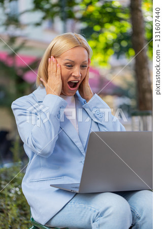 Happy mature businesswoman using laptop computer celebrating success victory clenching fists in city 131607440