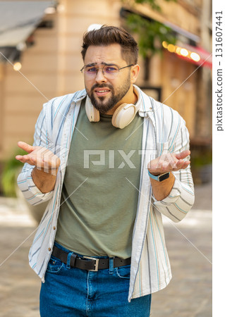 Doubtful sad frustrated young Caucasian man shrugging shoulders dont know answer on city street 131607441