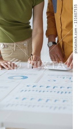 Two business professionals are collaborating on a project, analyzing financial charts and statistics displayed on a table, using a calculator for precise calculations. close up vertical view Two business professionals are collaborating on a project, analyzing financial charts and statistics displayed on a table, using a calculator for precise calculations. close up vertical view 131607535