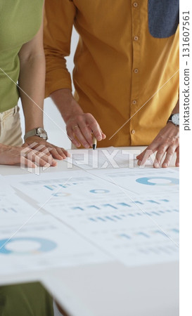 Business professionals analyzing financial reports, pointing at charts during collaborative meeting, discussing data with focused professional demeanor Business professionals analyzing financial reports, pointing at charts during collaborative meeting, discussing data with focused professional demeanor 131607561