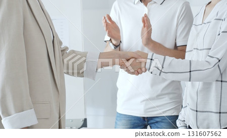 Professional businesswomen greeting, handshaking after closing deal, male coworker clapping in contemporary workplace setting. Business people concept 131607562