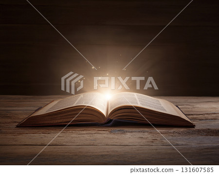 Open book emits magical glow on wooden table, creating enchanting atmosphere with sparkling lights 131607585