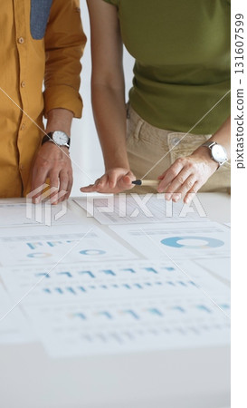 Business professionals analyzing financial reports, pointing at charts during collaborative meeting, discussing data with focused professional demeanor 131607599