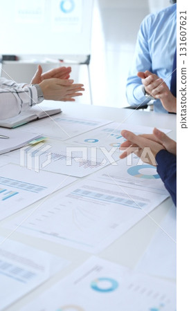 Business people team clapping hands in meeting celebrating success with financial charts, data analysis, sales growth reports, and teamwork achievement in modern office 131607621