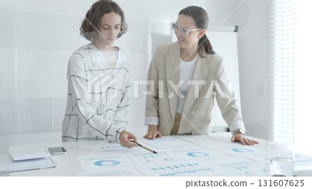 Two businesswomen are examining financial charts and statistics during a productive meeting in a modern office, demonstrating teamwork and strategic planning. Business people concept Two businesswomen are examining financial charts and statistics during a productive meeting in a modern office, demonstrating teamwork and strategic planning. Business people concept 131607625
