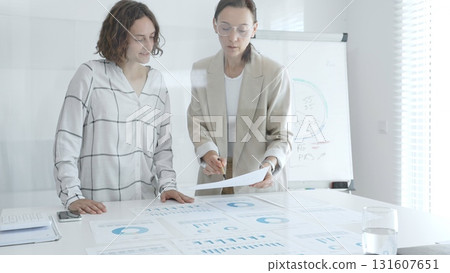 Professional businesswomen analyzing financial charts, collaborating in sleek corporate workspace, highlighting data. Business people concept 131607651
