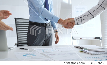 Business partnership success concept with handshake in modern office, financial charts, graphs and laptop on desk representing teamwork, agreement and corporate growth 131607652