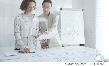 Two businesswomen analyzing financial reports and discussing growth strategies while collaborating in a modern office setting. Business people concept Two businesswomen analyzing financial reports and discussing growth strategies while collaborating in a modern office setting. Business people concept 131607659