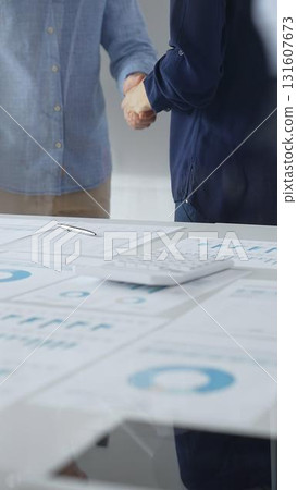 Professional businesspeople concluding deal, shaking hands near financial paperwork, calculator, pen on pristine workspace surface. Handshake concept 131607673