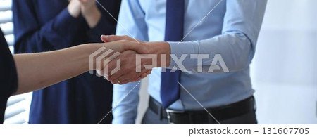 Professional business people shaking hands, concluding a successful partnership agreement and closing a significant deal in an office meeting 131607705