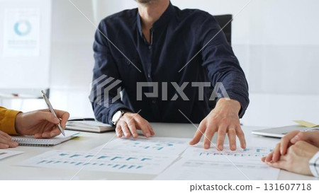 Professional colleagues reviewing financial charts, collaborating on strategic planning, gesturing toward data visualizations during corporate meeting in contemporary workspace 131607718