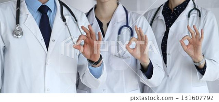 Medical team in white coats with stethoscopes making ok gestures, conveying teamwork, confidence, successful care and trust in a hospital or clinic setting 131607792