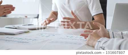 Professional team reviewing financial charts, collaborating intently around conference table in contemporary workspace, sharing insights during strategic planning session 131607807