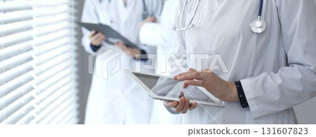 Medical professional using a digital tablet for patient care and data management, collaborating with doctors and healthcare workers in a modern clinic or hospital setting 131607823