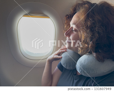 Happy passenger young woman is flying in plane. Smiling girl sitting in airplane near window going on trip vacation travel. Traveling female inside plane enjoying flight. Traveling girl 131607949