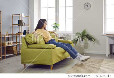 Happy, relaxed woman sitting on a comfortable green couch in the living room interior Happy, relaxed woman sitting on a comfortable green couch in the living room interior 131608018