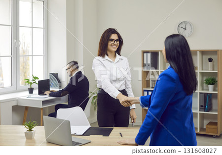 Two cheerful businesswomen shaking hands in modern office 131608027
