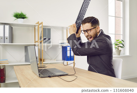 Angry shouting man working on workplace in office trying to destroy the monitor with his keyboard. 131608040