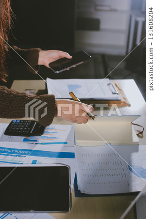 Close-up of businessman's hands making notes, mobiles, chart, desk, office 131608204
