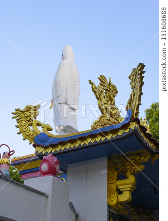 A white-robed sculpture and carved wooden gilded Asian dragons on the roof of the building A white-robed sculpture and carved wooden gilded Asian dragons on the roof of the building 131608688
