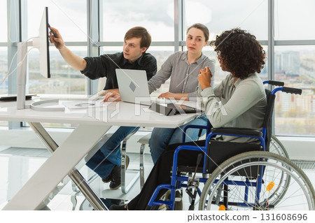 Teamwork brainstorm. Diverse multiracial colleagues woman in chair for people with disability working together. Group of people sitting in creative office discussing business. Young professional team 131608696