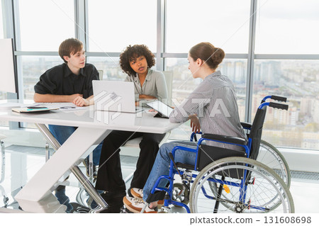 Teamwork brainstorm. Diverse multiracial colleagues woman in chair for people with disability working together. Group of people sitting in creative office discussing business. Young professional team 131608698