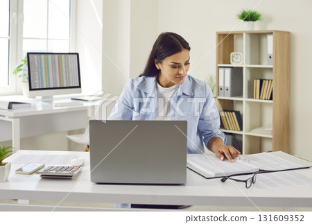 Female accountant working in her office, doing paperwork and using laptop computer 131609352