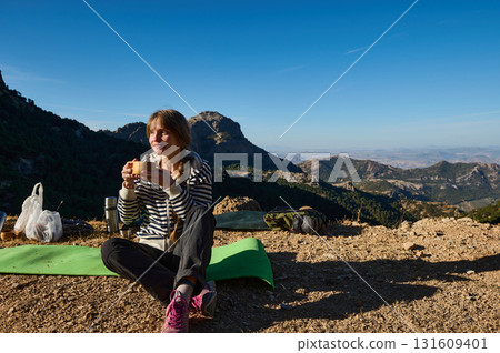 Woman Hiker Enjoying Snack On Mountain Summit With Backpack, Mat And Scenic Valley View 131609401