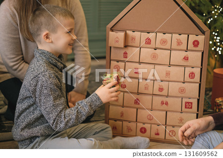 A child opens a box with a surprise Advent calendar surrounded by parents sitting on the floor by a Christmas tree 131609562