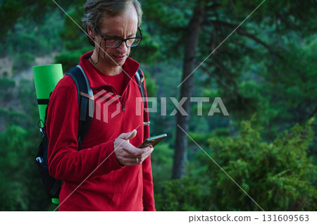 Hiker With Red Fleece Jacket Checking Smartphone On Forest Trail, Wearing Backpack With Green Sleeping Mat, Ready For Outdoor Adventure Hiker With Red Fleece Jacket Checking Smartphone On Forest Trail, Wearing Backpack With Green Sleeping Mat, Ready For Outdoor Adventure 131609563