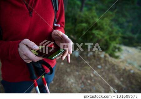 Hiker Using Smartphone On Forest Trail With Trekking Poles And Red Jacket Hiker Using Smartphone On Forest Trail With Trekking Poles And Red Jacket 131609575