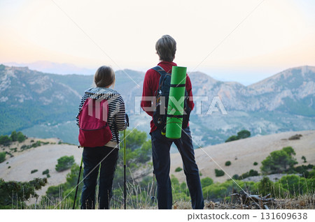Two Hikers With Backpacks Stand At Mountain Lookout At Sunset, Ready For Adventure Two Hikers With Backpacks Stand At Mountain Lookout At Sunset, Ready For Adventure 131609638