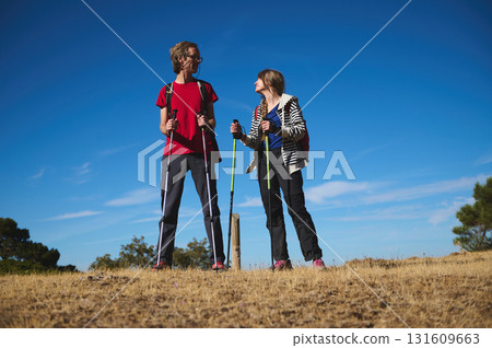 Two Hikers With Trekking Poles On a Hill Under a Bright Blue Sky Two Hikers With Trekking Poles On a Hill Under a Bright Blue Sky 131609663