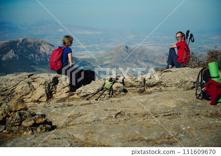 On a Mountain Summit, Friends Hike Together With Backpacks, Trekking Poles, and Dog Beneath Expansive Valley 131609670