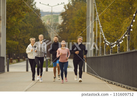 Team of people men and women running together along a bridge in city park. 131609752