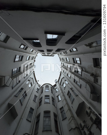Urban courtyard perspective looking up through tall grey buildings toward the sky 131609794