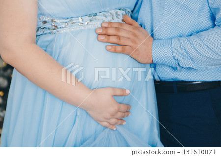 a man in a blue shirt hua man in a blue shirt hugs his wife's pregnant belly with his hand. girl in a blue dress. close up. High quality photo 131610071